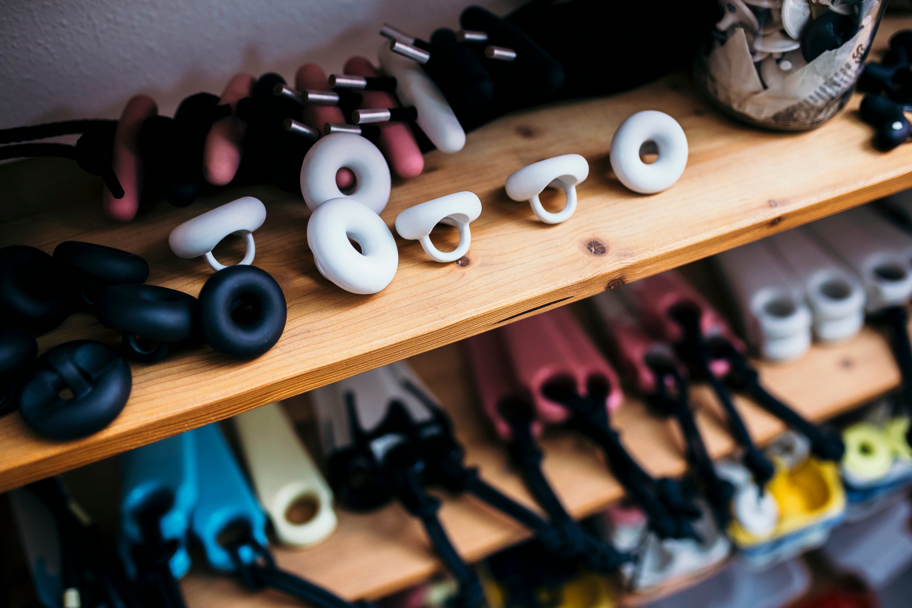White, unglazed porcelain donut ring accessories displayed on a wooden shelf, with additional black and pink versions blurred in the background.